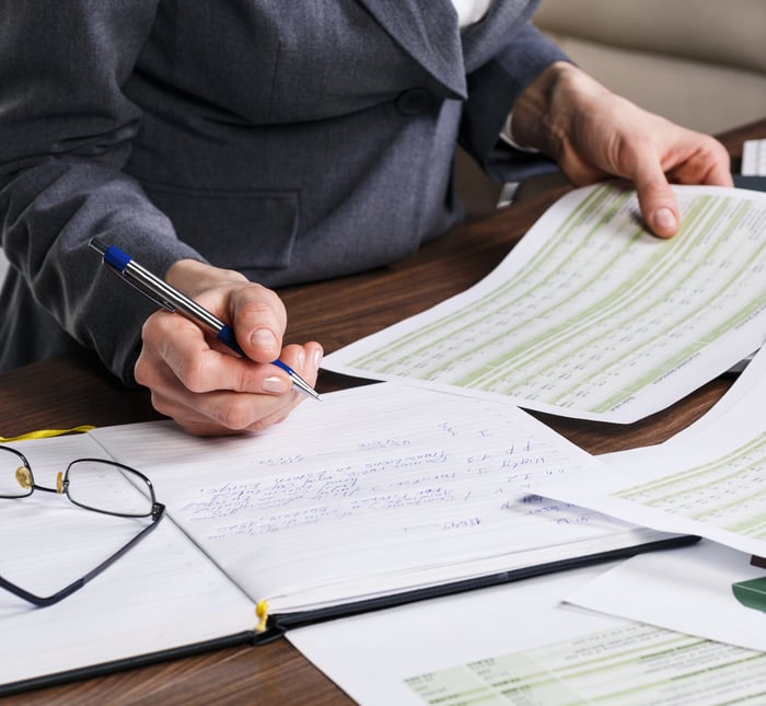 Close up of a woman holding financial documents and a pen reviewing papers at an office desk.