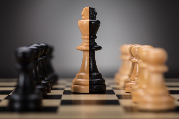 Chess pawn pieces are facing each other with a king piece in the center.