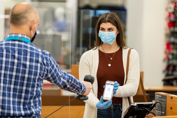 A Kohl's employee wearing a face mask scans a customer's phone for safe checkout.
