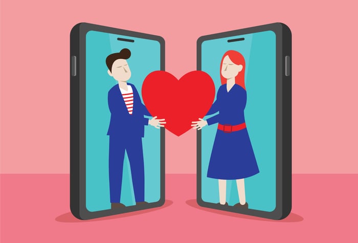 Cartoon of a man and a woman inside of two smartphones reaching out and holding a large red heart between them