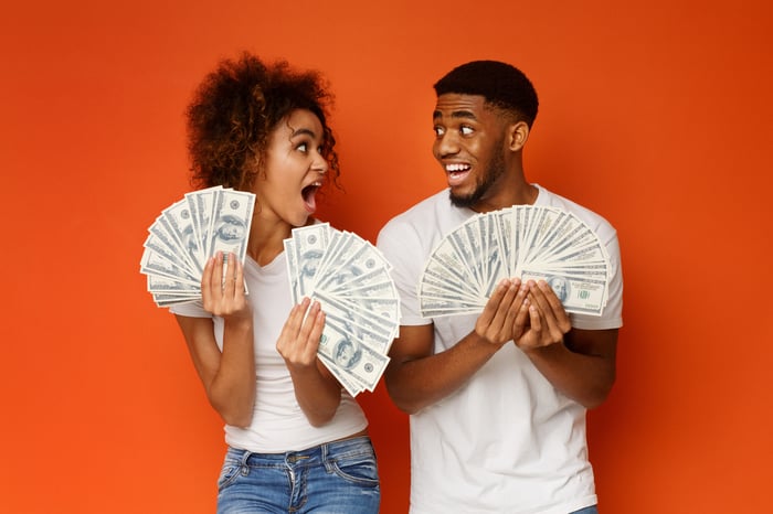 Excited younger man and woman fanning out hundred-dollar bills