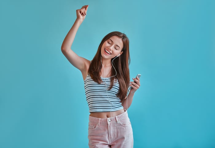 A young woman smiling while dancing to music on headphones.