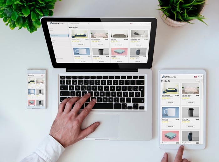 A man comparing an e-commerce page on a laptop, notebook, and smartphone app.