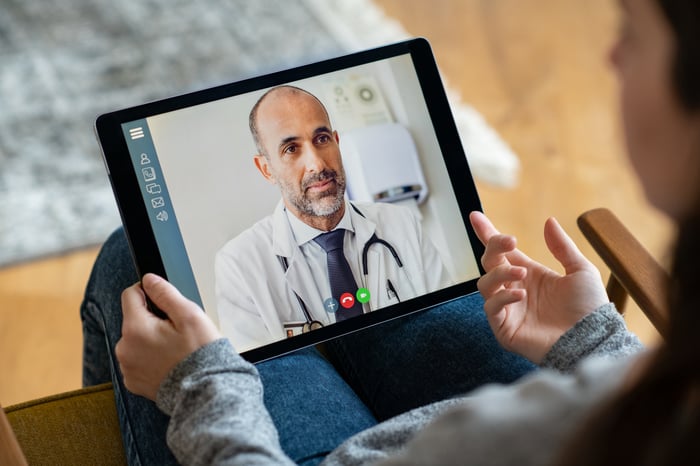 Young woman sitting in an armchair making a video call with her doctor. 