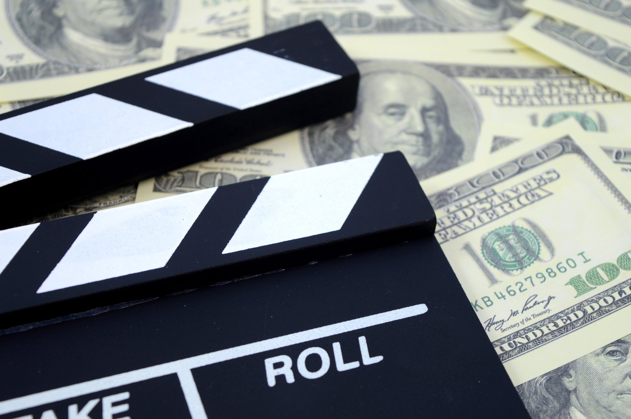 Movie production take and roll chalkboard atop a pile of $100 bills