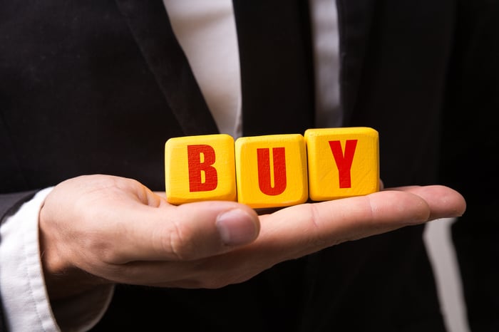 Man in a business suit holding blocks that spell out the word BUY.