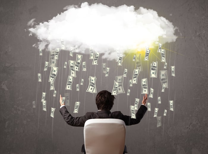 A businessman catches cash raining from a cloud.