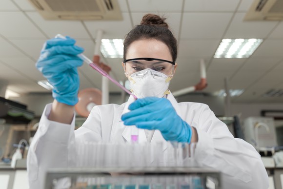 A lab technician with a pipette and pink liquid.
