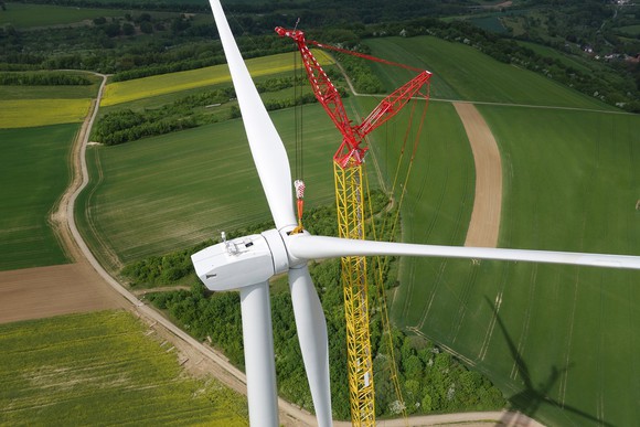 Crane installing blades on wind turbine.