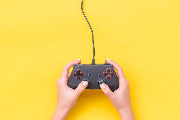 A pair of hands holding a video game controller on a yellow background