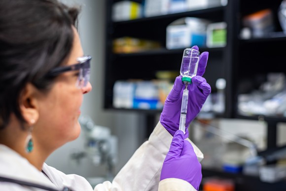 Woman in medical gear fills syringe from a vial