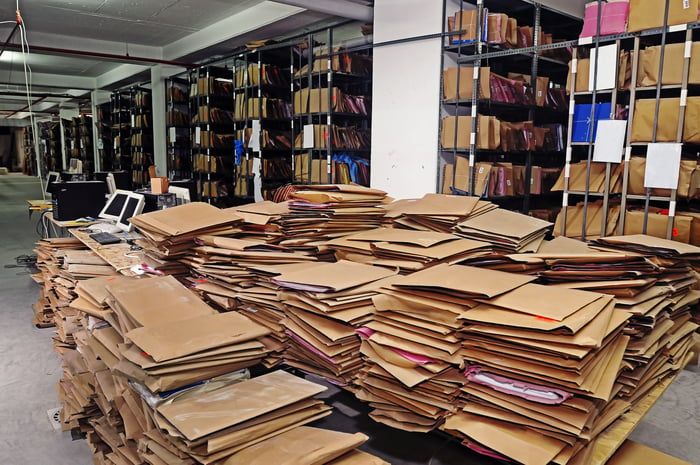 A mess of paper files on the ground, with rows of file storage racks in the background