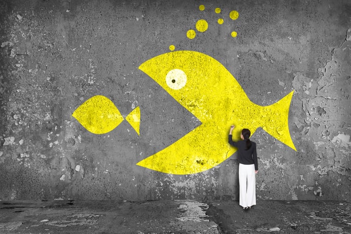 Person finishing up a wall painting that depicts a large yellow fish eating a smaller yellow fish.