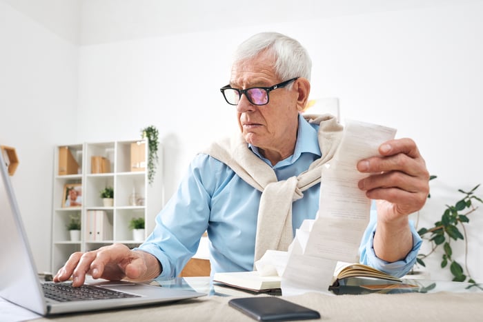 Older man at laptop holding receipt