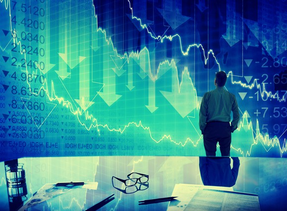 A dejected person looking at a stock chart with downward pointing arrows