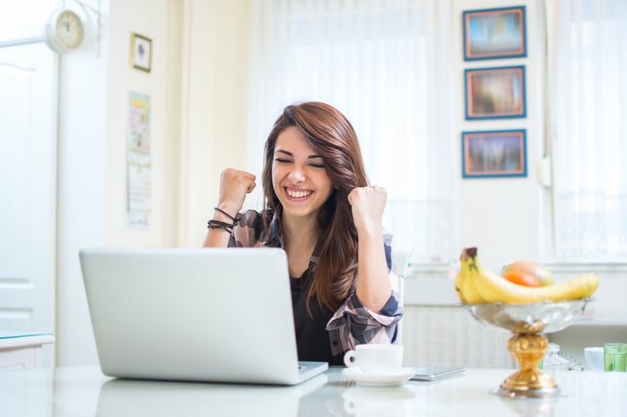 Excited young woman with two fists raised as she looks at her laptop