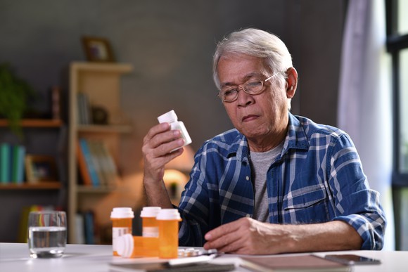 Elderly person at a table with bottles of pills.