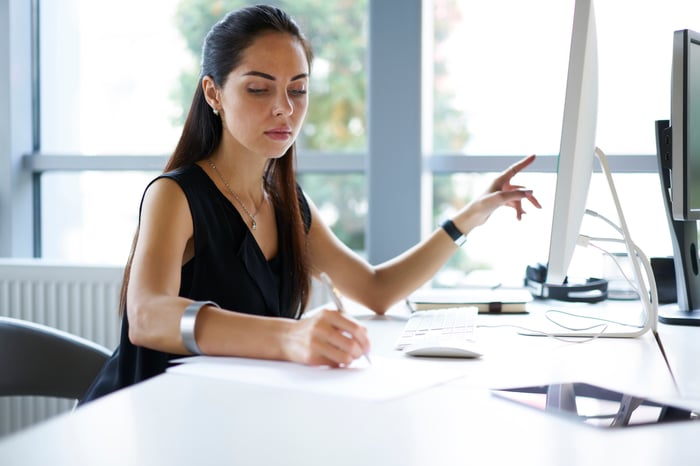 Woman using checklist to compare against the information on her computer. 