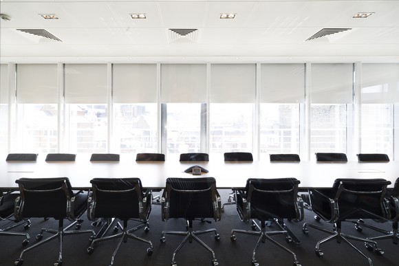 An ultramodern corporate boardroom with rows of chairs flanking a long polished tabletop.