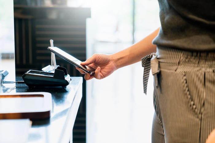 A person holding a smartphone near a touchless, digital payment terminal.