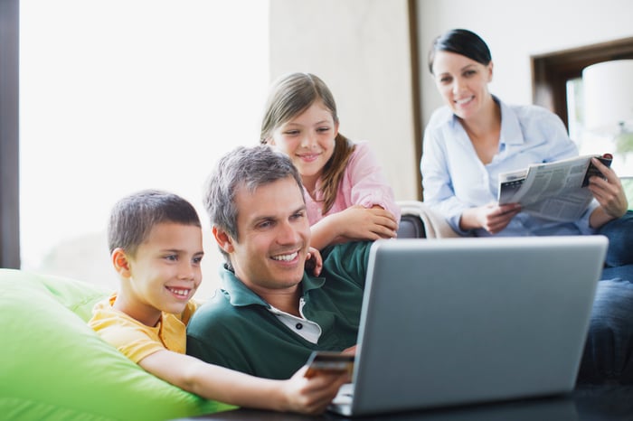 Smiling family huddled around laptop with a young boy holding a credit card.