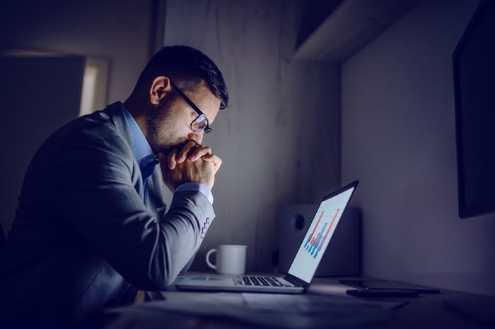 Man with serious expression staring at graph on laptop screen