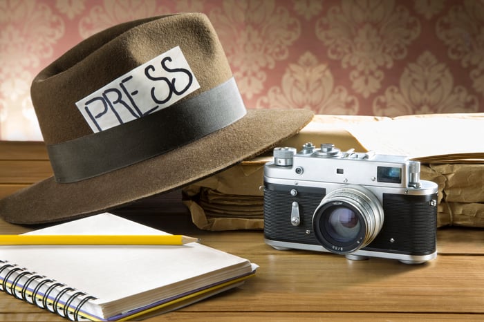 Press sign on a fedora next to a notebook and camera