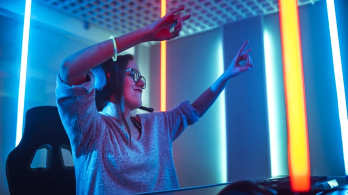 Female gamer seated at a PC raising hands in triumph.