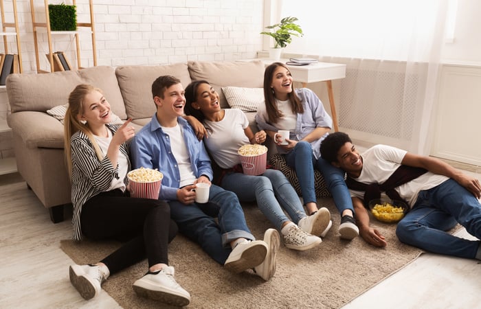 Smiling group of young adults watching television and eating popcorn.