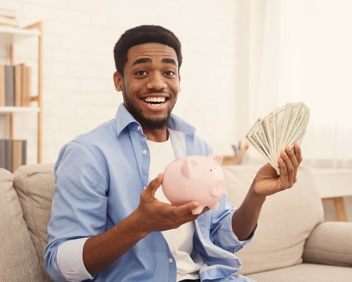 Smiling man with lots of cash and a piggy bank