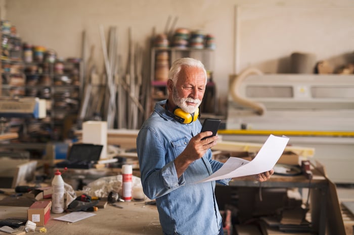 Older person holding document and looking at phone in workshop.