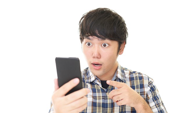 A young man is gawking at his smartphone, with his mouth ajar.