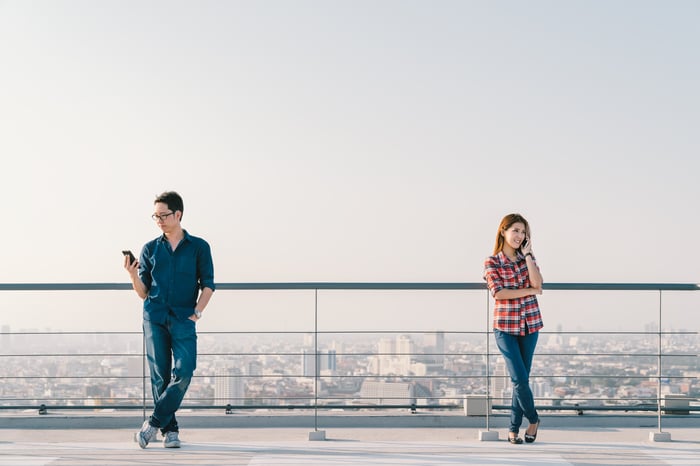 A man and a woman use smartphones outside.