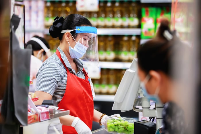 Woman scanning food at register, wearing a mask and gloves.