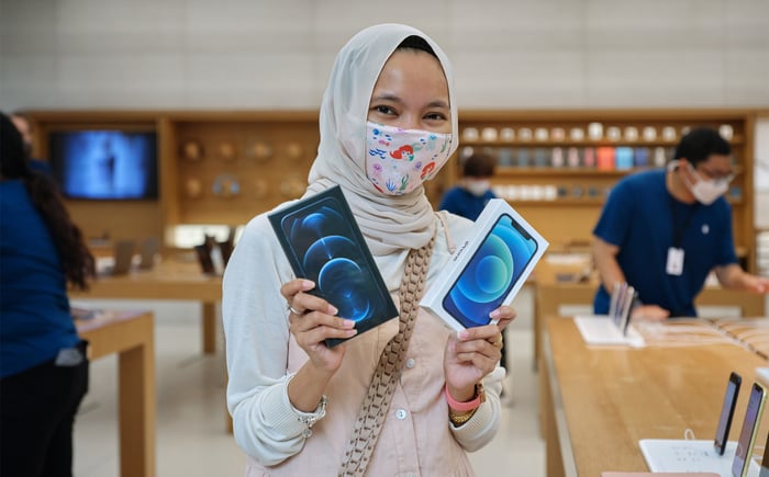 Female customer in Apple store holding up two boxed iPhone 12 models