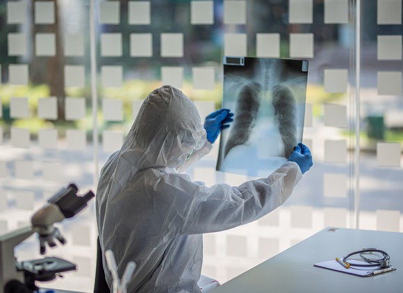 A doctor in protective gear studying a patient's chest x-ray.