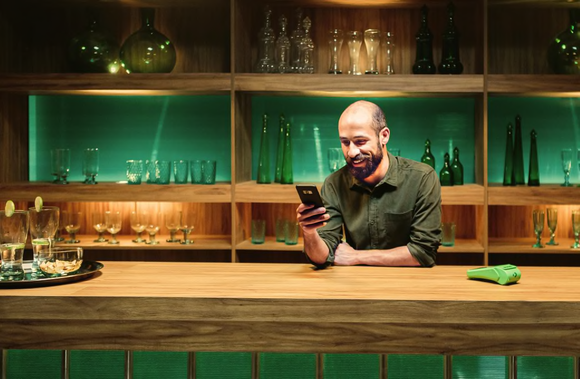 Merchant leaning on a counter with glassware on shelves behind him and a Stone card-reading machine next to him