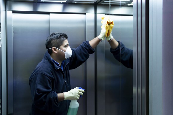 A hotel worker in a mask cleaning the interior of an elevator.