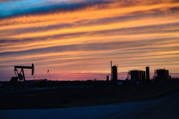 An oil pump at dusk with rows of clouds in the sky.