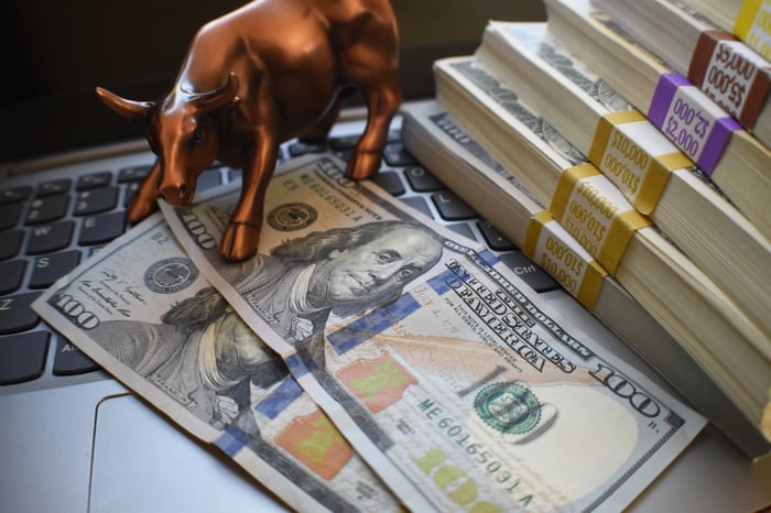 Stacks of $100 bills and a small, bronze bull statue on a computer keyboard, 