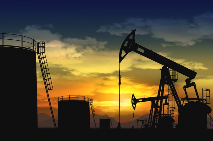 Oil pumps and storage tanks with the sun setting in the background.