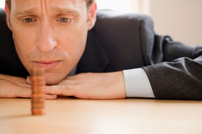 A businessman pensively staring at a neat stack of pennies. 