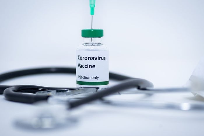 Small vial with "Coronavirus vaccine" written on it and a stethoscope sitting on a flat white surface.