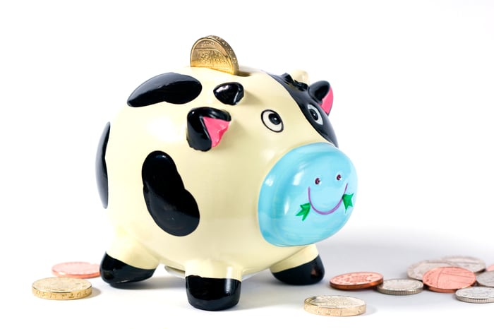 A cow colored piggy bank with coins around it.