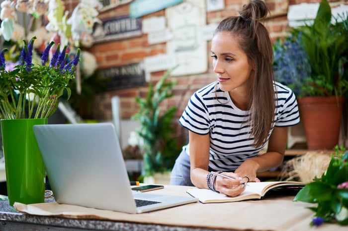 Business owner writing in a book and looking at a computer in a florist shop.