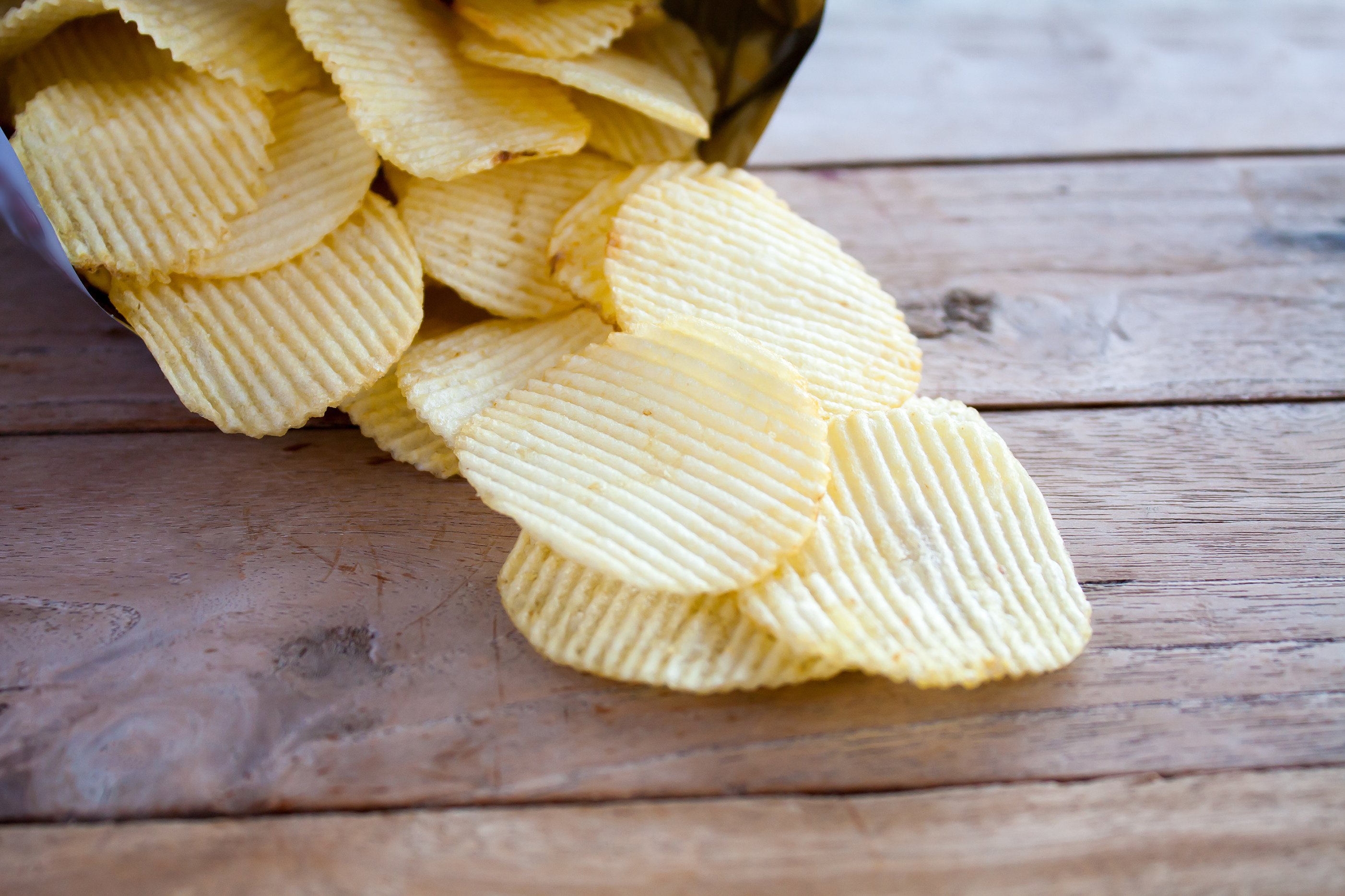 Open bag of potato chips pouring onto a picnic table
