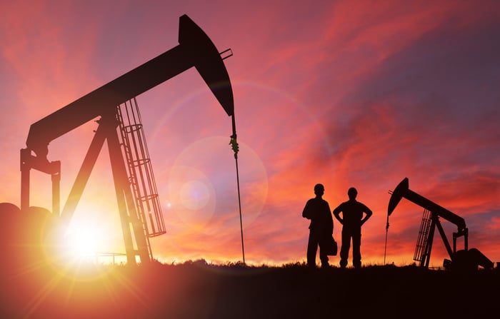 Two men in silhouette with oil rigs.