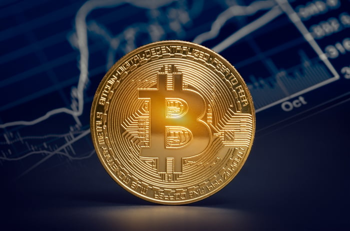 Bitcoin emas fisik berdiri di depan grafik digital. 