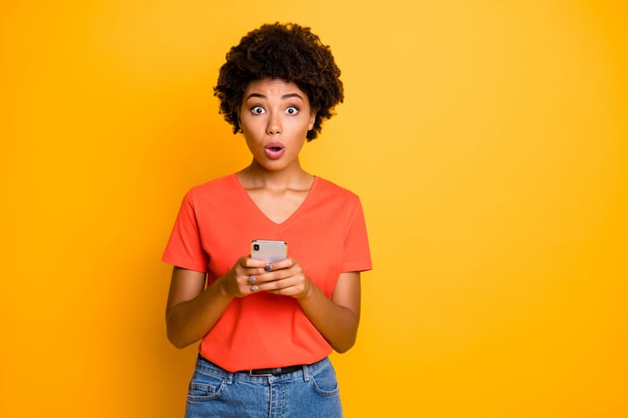 With a surprised expression, a woman holds a cell phone.