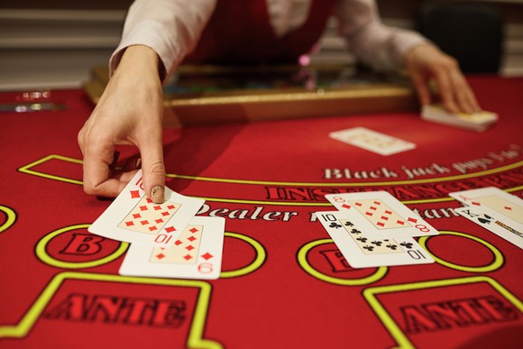 A dealer dealing cards face-up on a red tabletop with yellow markings.
